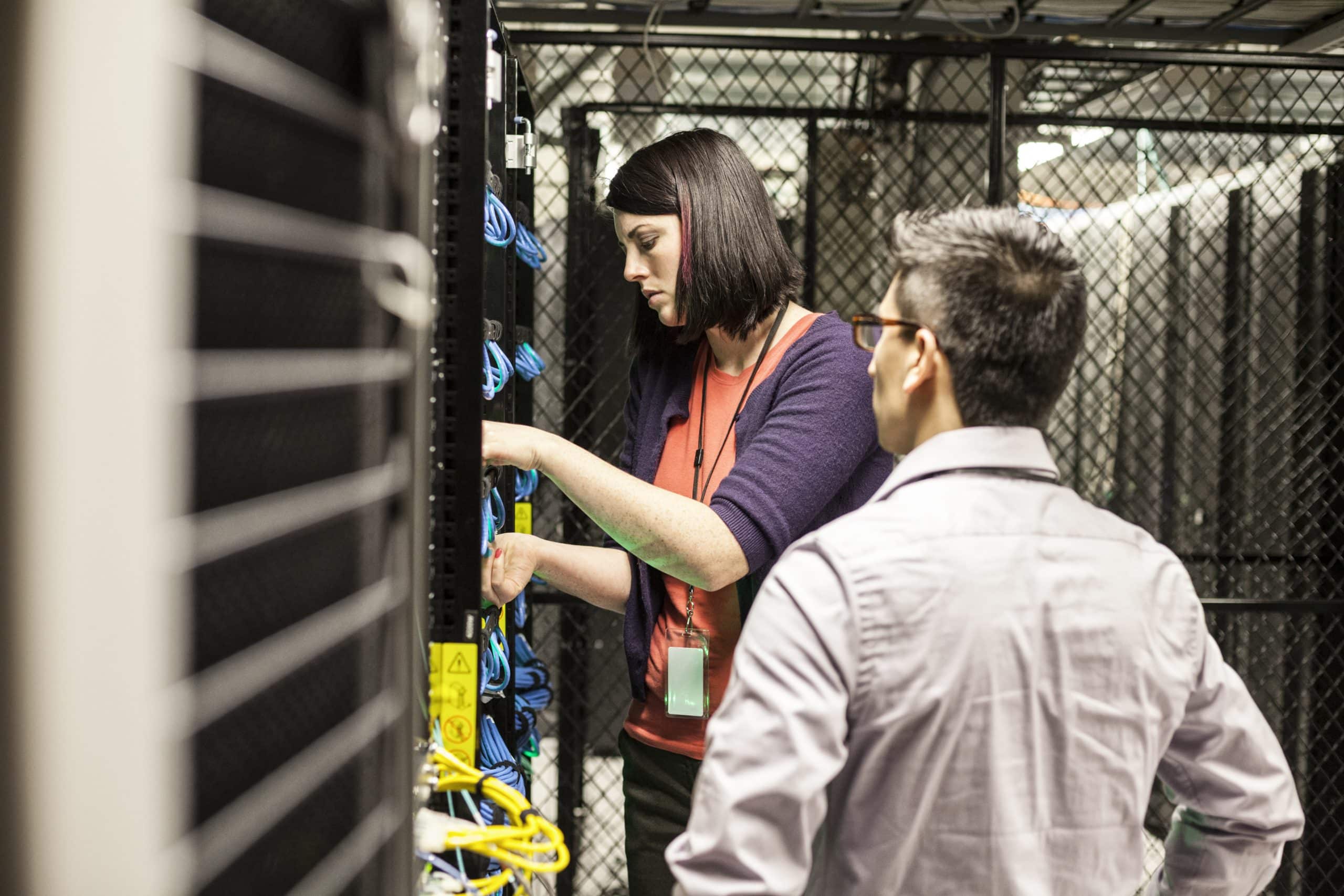 Caucasian woman and man technicians working on CAT 5 cables in a large computer server farm. UniFi Network Design & Installation technicians